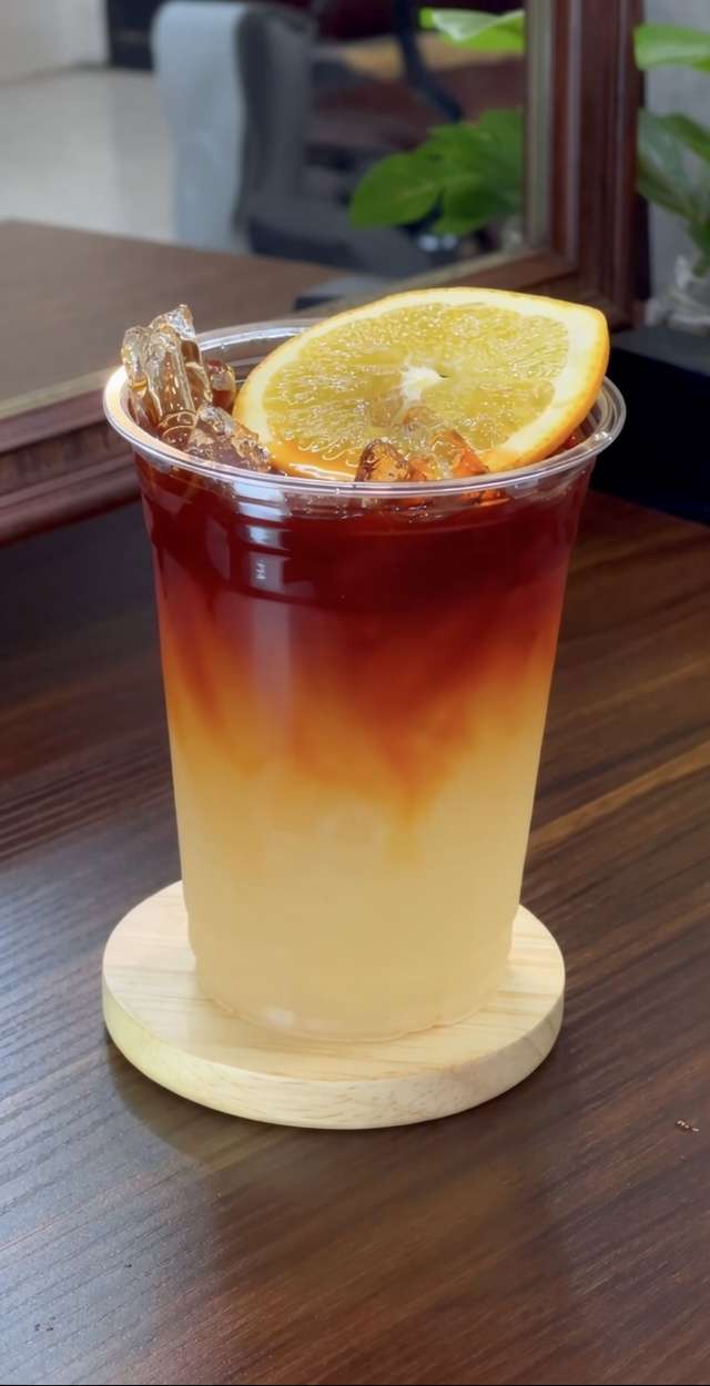 Iced lemon tea lemonade served in tall glasses with fresh lemon slices, orange slices, ice cubes, black tea layer, and mint leaves.
