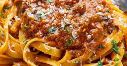 Tagliatelle Bolognese served with rich ground beef tomato sauce, grated parmesan, chopped parsley, and black pepper on top.