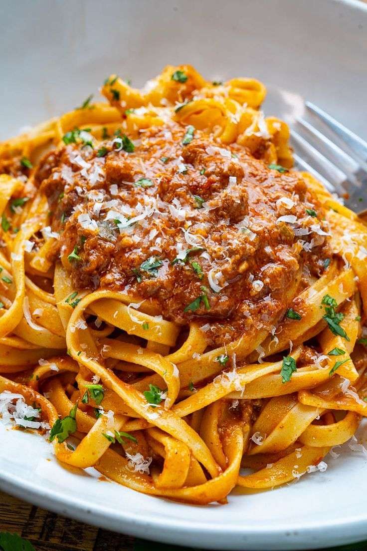 Tagliatelle Bolognese served with rich ground beef tomato sauce, grated parmesan, chopped parsley, and black pepper on top.