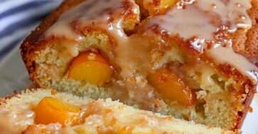 Peach loaf cake with vanilla glaze, sliced peaches on top, soft golden crumb, and diced peach pieces inside, served on a plate.