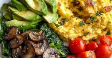 Healthy scrambled egg breakfast plate with creamy scrambled eggs, avocado slices, sautéed mushrooms, spinach, cherry tomatoes, parsley, and chili flakes.