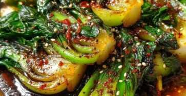 Spicy garlic soy bok choy served hot with sesame seeds, glossy soy chili sauce, minced garlic, ginger, and bright green leaves.