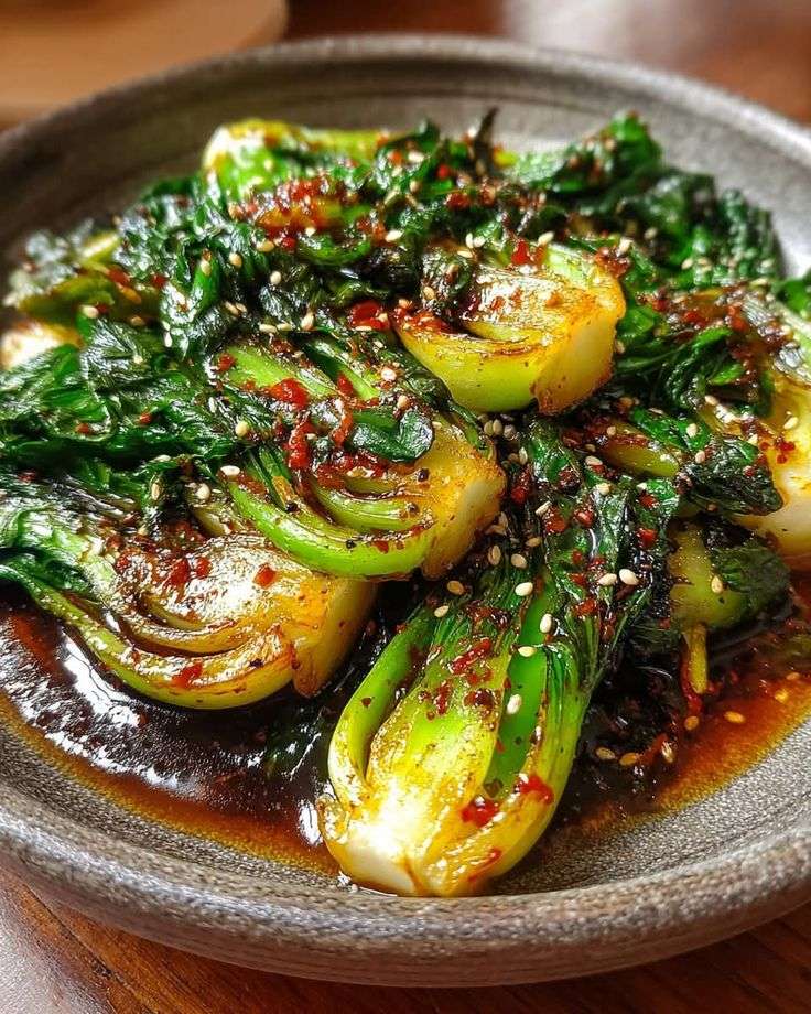 Spicy garlic soy bok choy served hot with sesame seeds, glossy soy chili sauce, minced garlic, ginger, and bright green leaves.