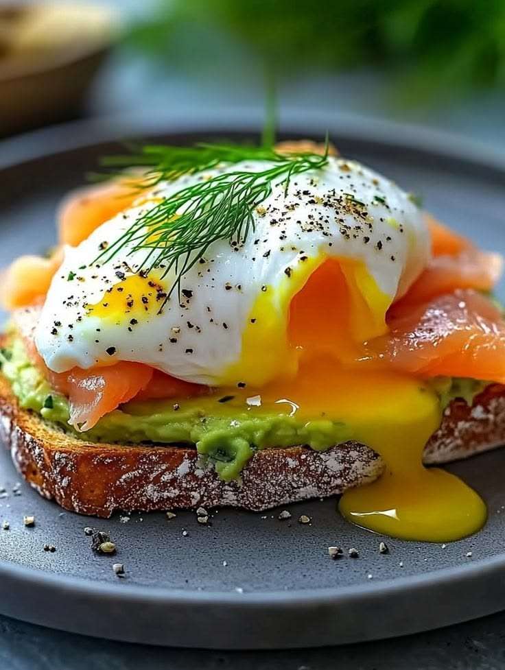 Avocado toast topped with smoked salmon, poached egg, fresh dill, black pepper, chili flakes, lemon, and crispy sourdough bread.