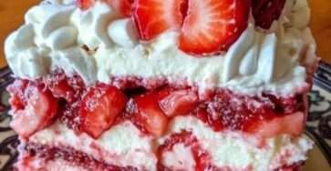 A spectacular four-layer red velvet cake filled with bright white cream cheese frosting and sliced strawberries, displayed elegantly on a glass cake stand.