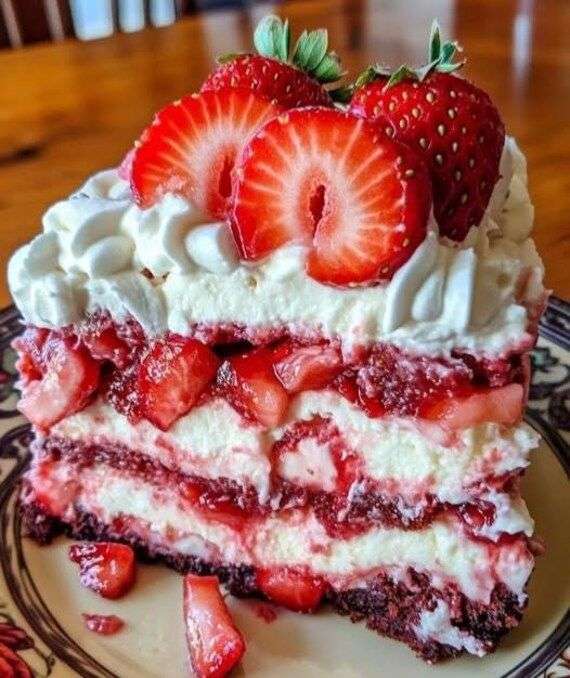 A spectacular four-layer red velvet cake filled with bright white cream cheese frosting and sliced strawberries, displayed elegantly on a glass cake stand.