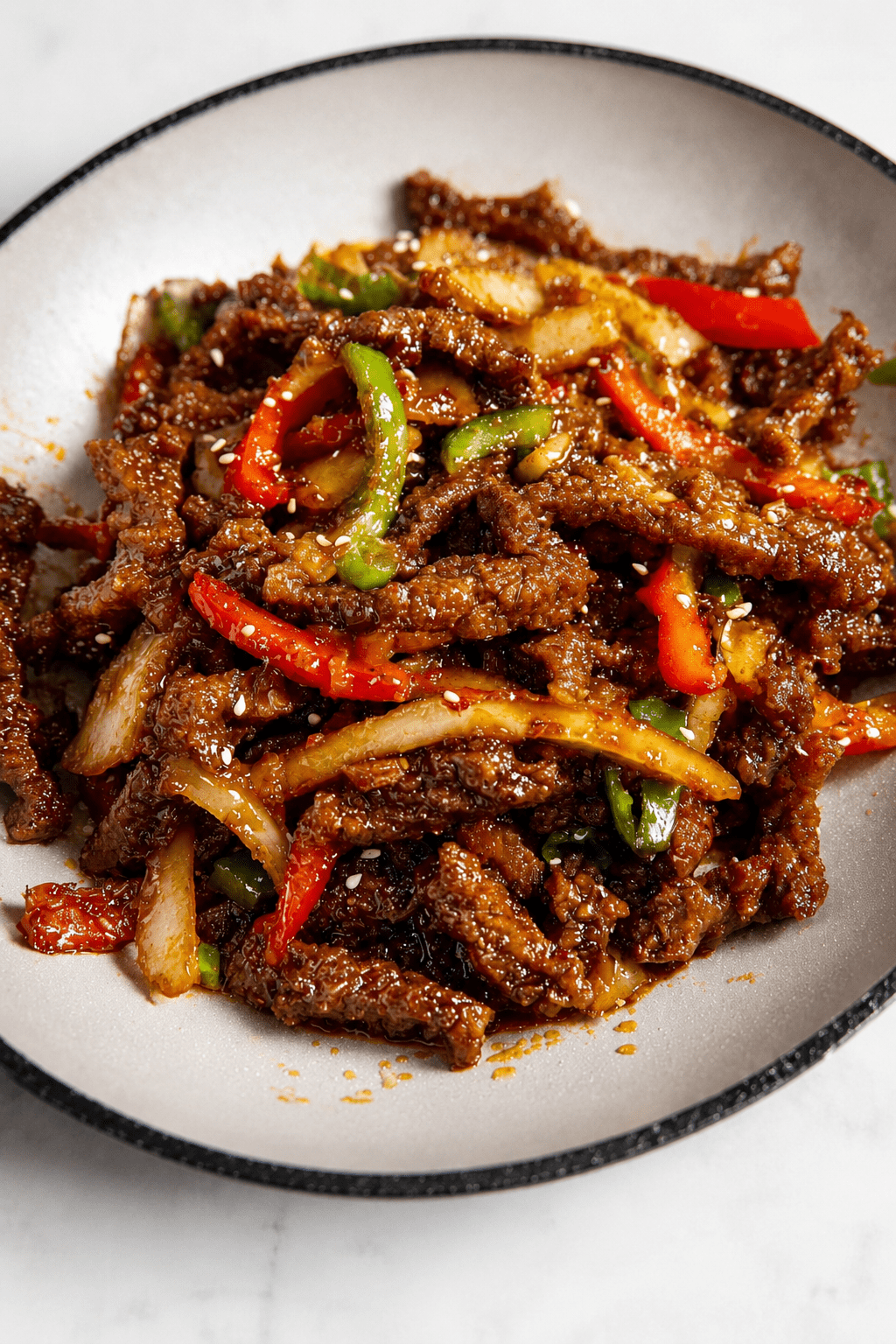 Crispy chilli beef stir-fry served with sliced bell peppers, onion, sesame seeds, and a glossy sweet spicy sauce over rice.