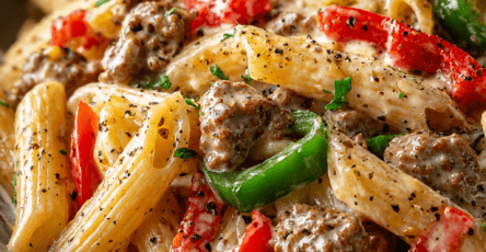 Creamy sausage and pepper penne pasta served in a bowl with red and green bell peppers, Parmesan cheese, fresh parsley, and black pepper.