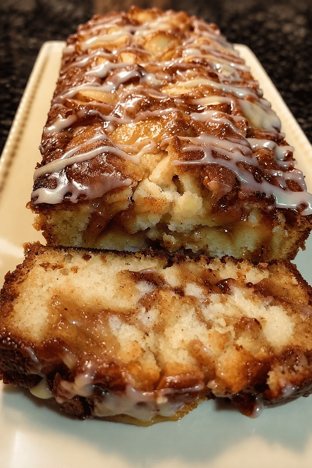 A sliced glazed apple cinnamon loaf cake with diced apples, cinnamon swirl filling, vanilla glaze, and a moist golden crumb on a serving plate.