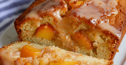 A sliced glazed peach loaf cake with fresh peach pieces, soft vanilla crumb, glossy glaze, and peach slices on top.