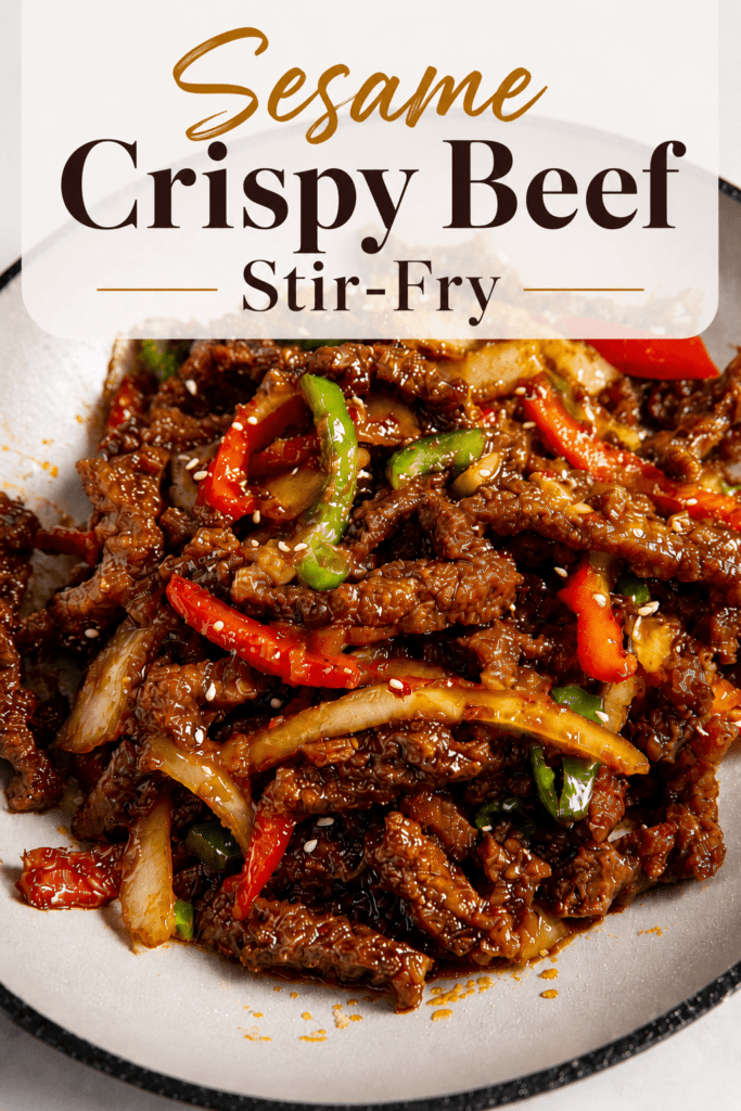 Crispy chilli beef stir-fry served with sliced bell peppers, onion, sesame seeds, and a glossy sweet spicy sauce over rice.