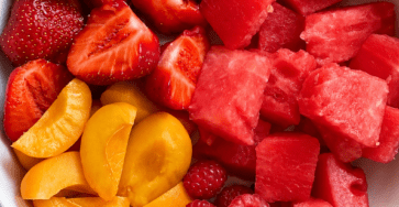 Fresh summer fruit salad with sliced strawberries, watermelon cubes, peaches, raspberries, mint, and a glossy honey-lime dressing in a bowl.