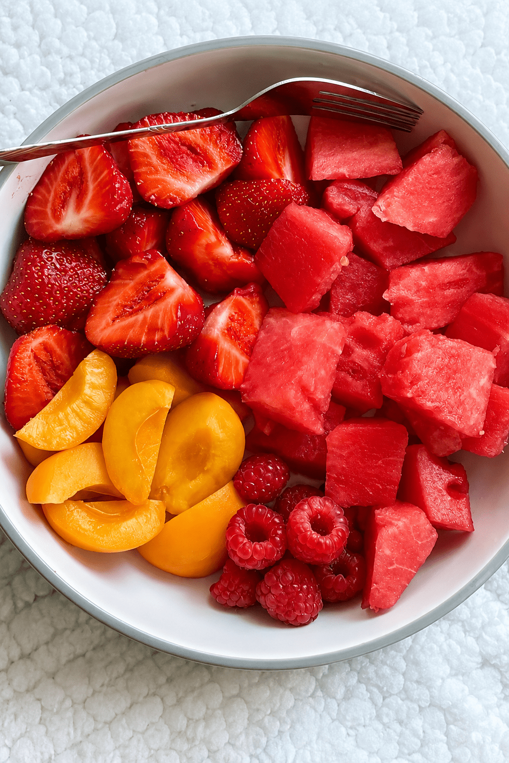 Fresh summer fruit salad with sliced strawberries, watermelon cubes, peaches, raspberries, mint, and a glossy honey-lime dressing in a bowl.