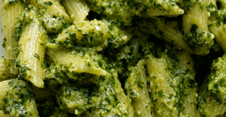 Creamy pesto penne pasta served in a bowl with fresh basil, Parmesan cheese, black pepper, and a bright green creamy pesto sauce.