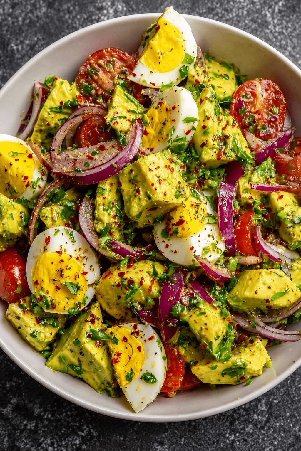 Avocado egg salad with boiled eggs, cherry tomatoes, red onion, fresh herbs, chili flakes, and lemon Dijon olive oil dressing.