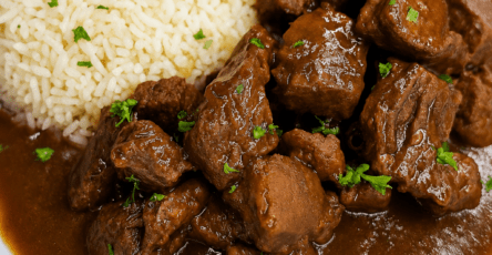 Tender beef stew with glossy brown gravy served beside fluffy white rice, garnished with fresh parsley on a dinner plate.