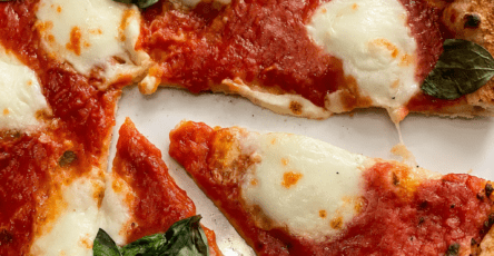 Homemade Margherita pizza with a golden puffed crust, fresh tomato sauce, melted mozzarella, basil leaves, olive oil, and cracked black pepper.