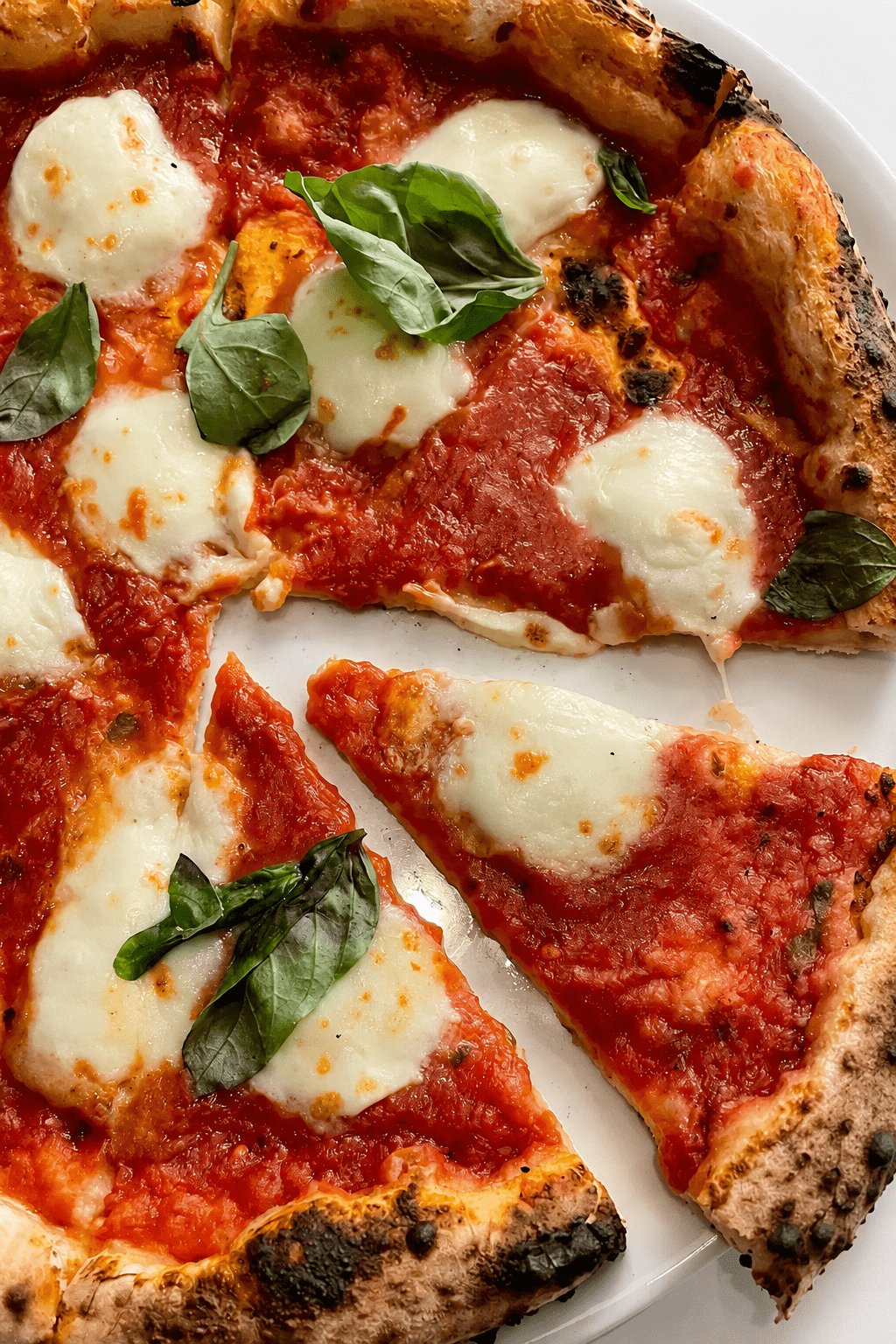 Homemade Margherita pizza with a golden puffed crust, fresh tomato sauce, melted mozzarella, basil leaves, olive oil, and cracked black pepper.