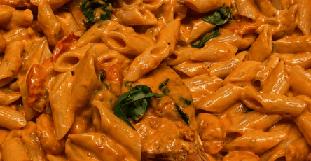 Creamy Tuscan chicken penne served in a bowl with golden chicken pieces, penne pasta, spinach, cherry tomatoes, parmesan, and a rich creamy tomato sauce.