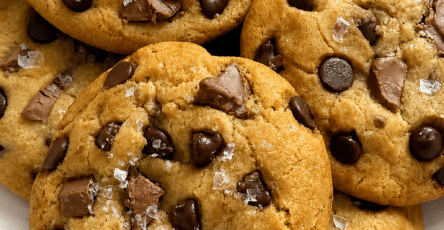 Soft chocolate chip cookies with golden edges, gooey chocolate chunks, dark chocolate chips, and flaky sea salt cooling on a baking tray.