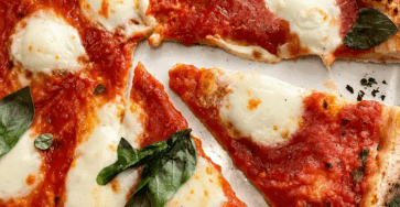 Homemade Margherita pizza with golden airy crust, red tomato sauce, melted fresh mozzarella, basil leaves and a drizzle of olive oil.