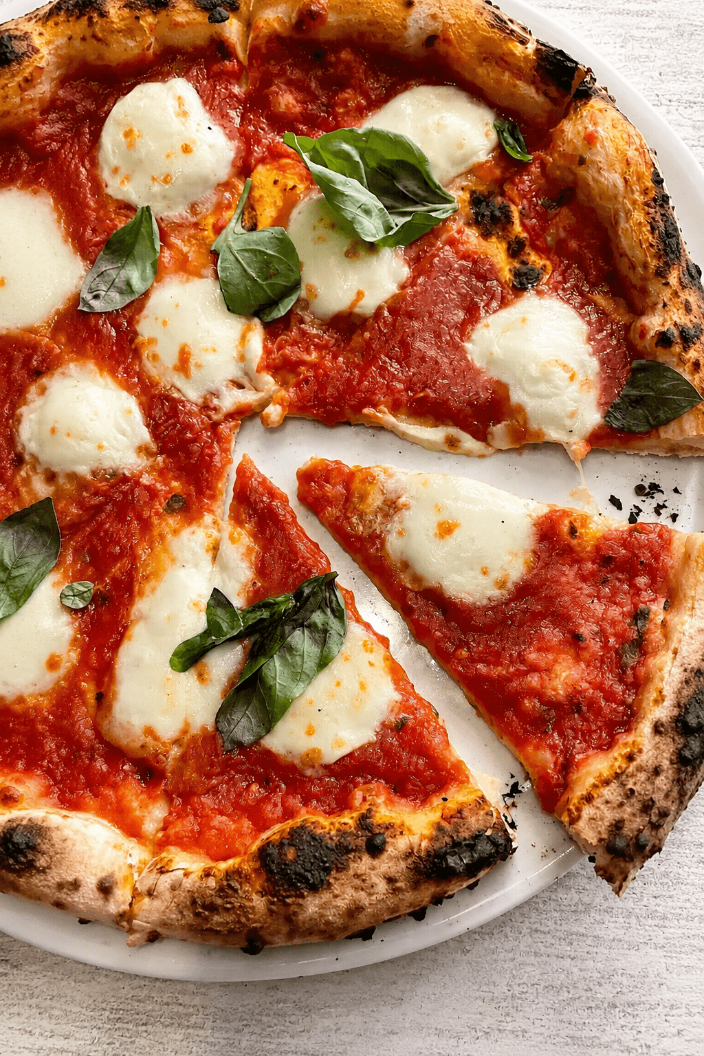 Homemade Margherita pizza with golden airy crust, red tomato sauce, melted fresh mozzarella, basil leaves and a drizzle of olive oil.