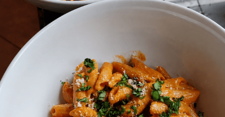 A bowl of creamy tomato penne pasta coated in a smooth pink tomato cream sauce, topped with grated parmesan and fresh basil.