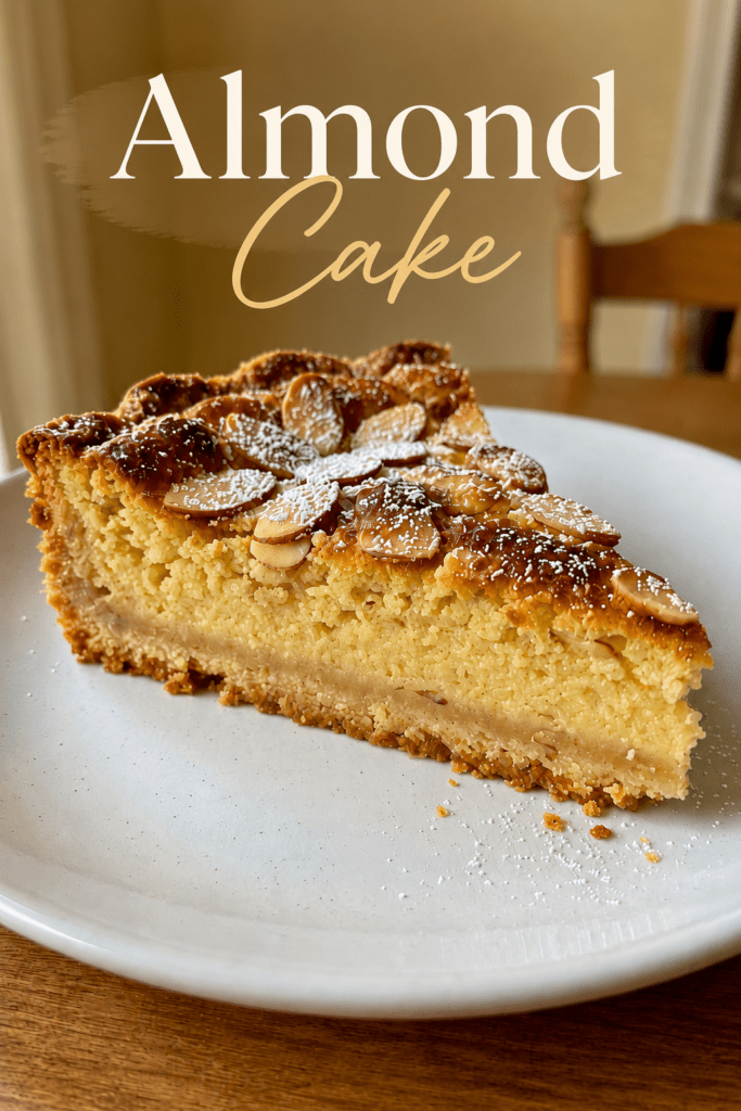 A golden almond custard tart with a buttery crust, creamy almond filling, sliced almonds on top and a dusting of powdered sugar.
