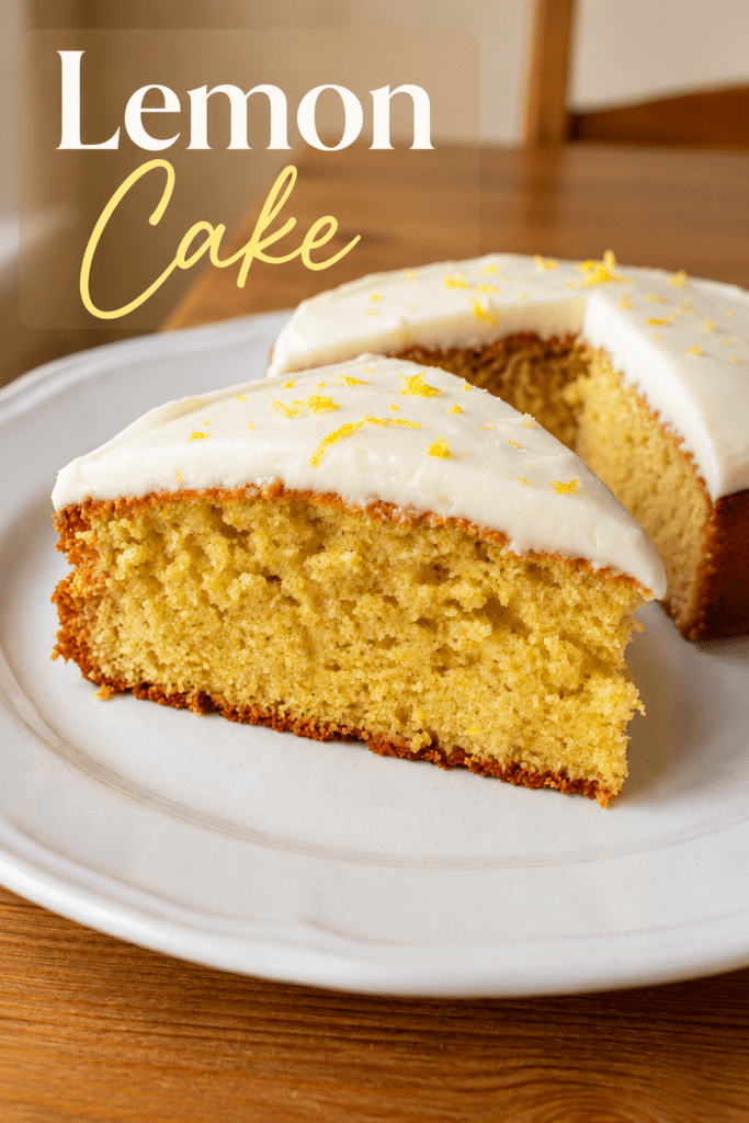 A soft lemon cake topped with smooth cream cheese frosting, fresh lemon zest and a moist golden crumb served on a cake plate.