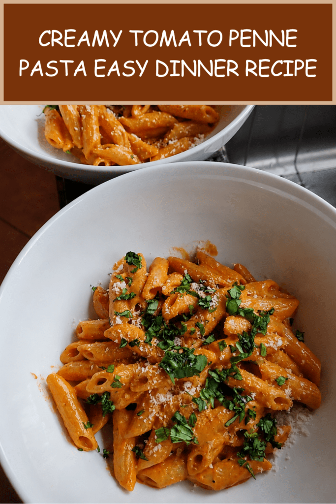 A bowl of creamy tomato penne pasta coated in a smooth pink tomato cream sauce, topped with grated parmesan and fresh basil.
