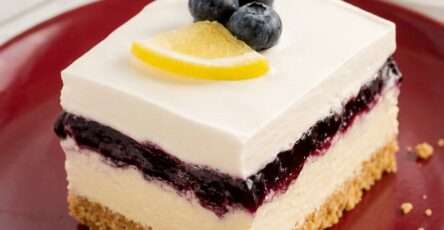 Sugar-free lemon blueberry delight dessert with a graham-style crust, creamy lemon cheesecake layer, blueberry topping, and whipped topping in a pan.