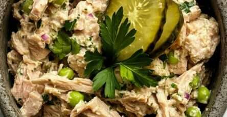 Creamy tuna salad served in a bowl with green peas, sliced pickles, red onion, parsley, and a smooth lemon mayonnaise dressing.