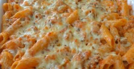 A golden baked pasta gratin with ground meat, tomato sauce, melted cheese, penne pasta, and fresh parsley in a rustic oven dish.