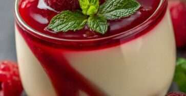 Creamy raspberry panna cotta served in small glasses with raspberry coulis, fresh raspberries, and mint leaves on top.