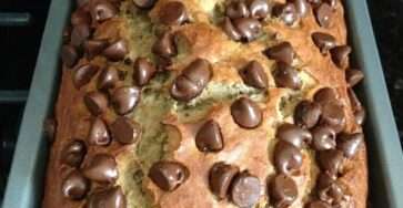 A freshly baked chocolate chip banana bread loaf sliced on a plate, showing a soft moist crumb with melted chocolate chips on top.