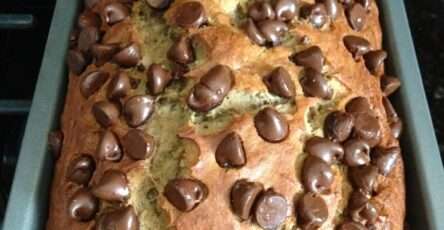 A freshly baked chocolate chip banana bread loaf sliced on a plate, showing a soft moist crumb with melted chocolate chips on top.