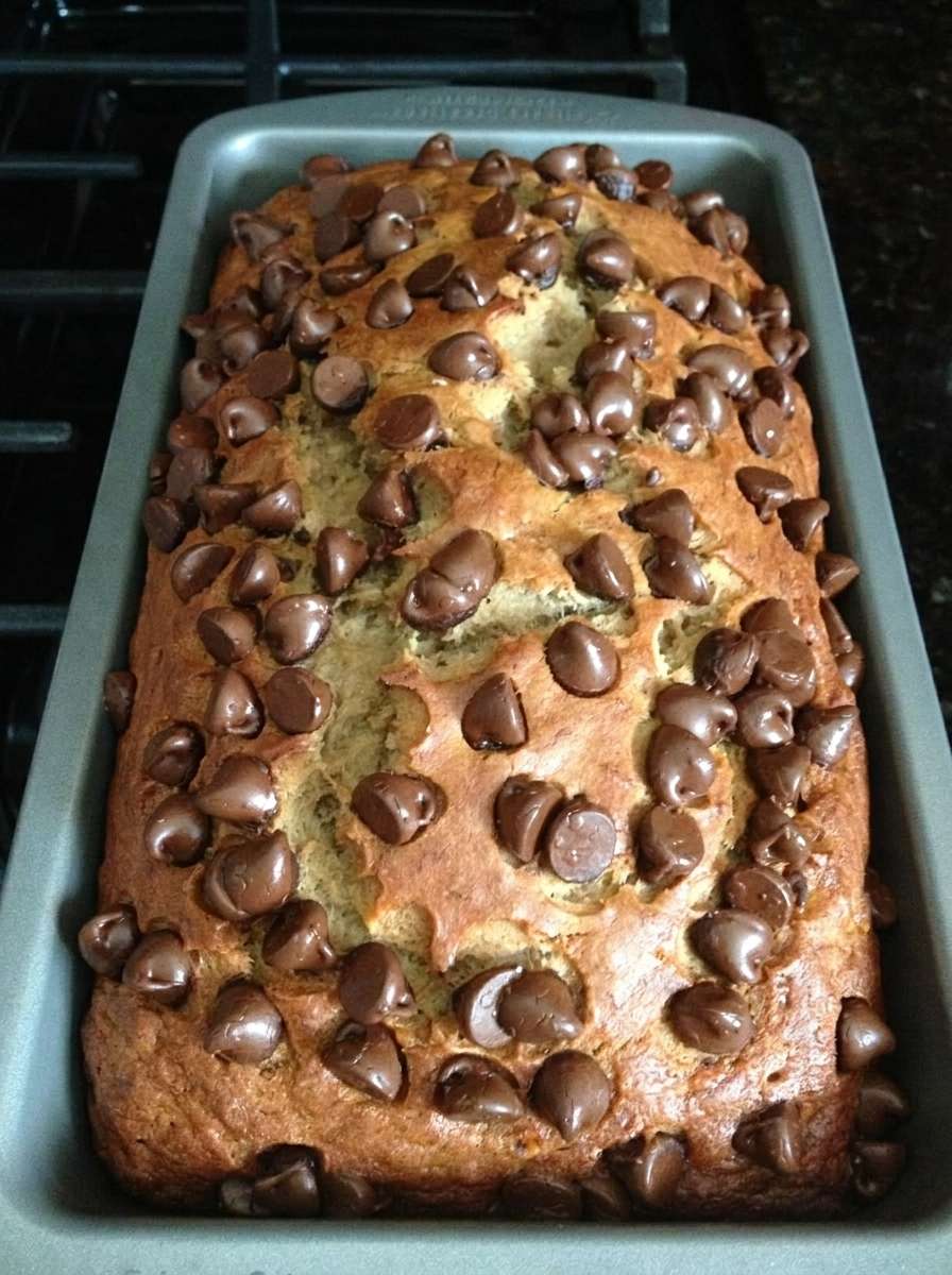 A freshly baked chocolate chip banana bread loaf sliced on a plate, showing a soft moist crumb with melted chocolate chips on top.