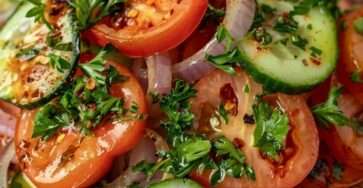 A fresh tomato cucumber onion salad served on a plate with sliced ripe tomatoes, cucumber rounds, thin red onion, parsley, olive oil dressing, and herbs.