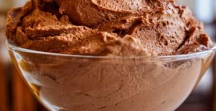 A clear glass footed coupe bowl filled with rich sugar-free chocolate mousse fluff, airy whipped texture, deep cocoa color, and a smooth sculpted top.