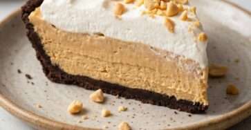 A creamy sugar-free no bake peanut butter pie in a dark chocolate cookie crust, topped with whipped cream swirls and chopped peanuts.