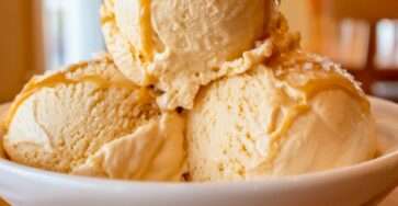 A white bowl filled with creamy sugar-free salted caramel ice cream scoops, drizzled with caramel sauce and finished with coarse sea salt flakes.