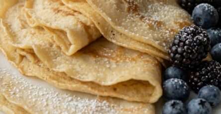 Thin sugar-free almond flour crepes folded into quarters on a plate, soft and golden, served as a low-carb breakfast or brunch recipe.