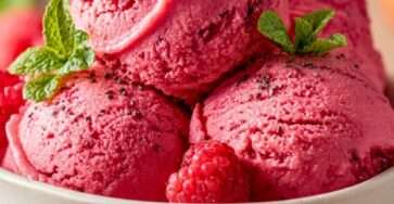 A bowl of sugar-free raspberry chia sorbet with a smooth bright pink texture, fresh raspberries, chia seeds, and mint leaves served cold.