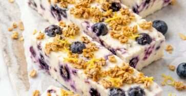 Blueberry lemon frozen yogurt bars cut into squares with creamy yogurt, whole blueberries, lemon zest and crunchy granola topping.