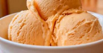 A scoop of sugar-free orange cream sherbet with a smooth creamy texture, bright orange color, fresh orange zest, and a refreshing frozen citrus finish.