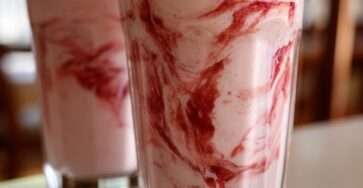 Sugar-free strawberry glaze smoothie served in clear glasses with a thick pink smoothie base, glossy strawberry swirl, and fresh strawberry topping.