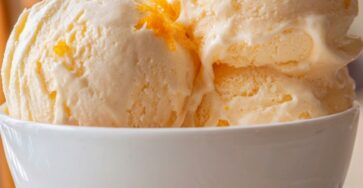 Sugar-free orange creamsicle ice cream scooped into a bowl with fresh orange zest, creamy pale orange texture, and a smooth frozen finish.