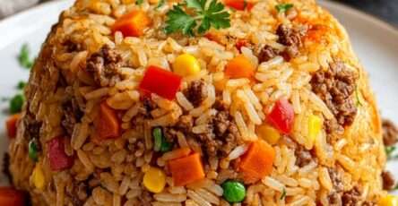Homemade ground beef fried rice shaped into a dome with carrots, peas, sweetcorn, red pepper, scrambled eggs, and chopped spring onions on a white plate.