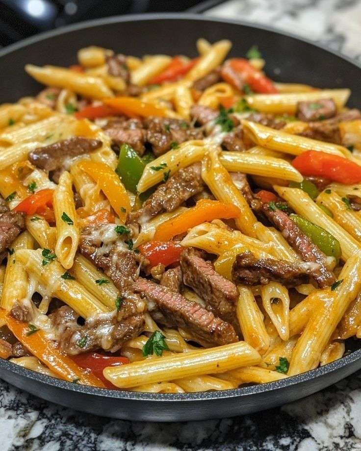 Creamy steak fajita pasta with penne, tender steak strips, red yellow and green bell peppers, melted cheese, and fresh parsley in a skillet.