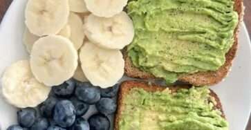 Healthy avocado toast on whole wheat bread served with banana slices and fresh blueberries on a simple breakfast plate.